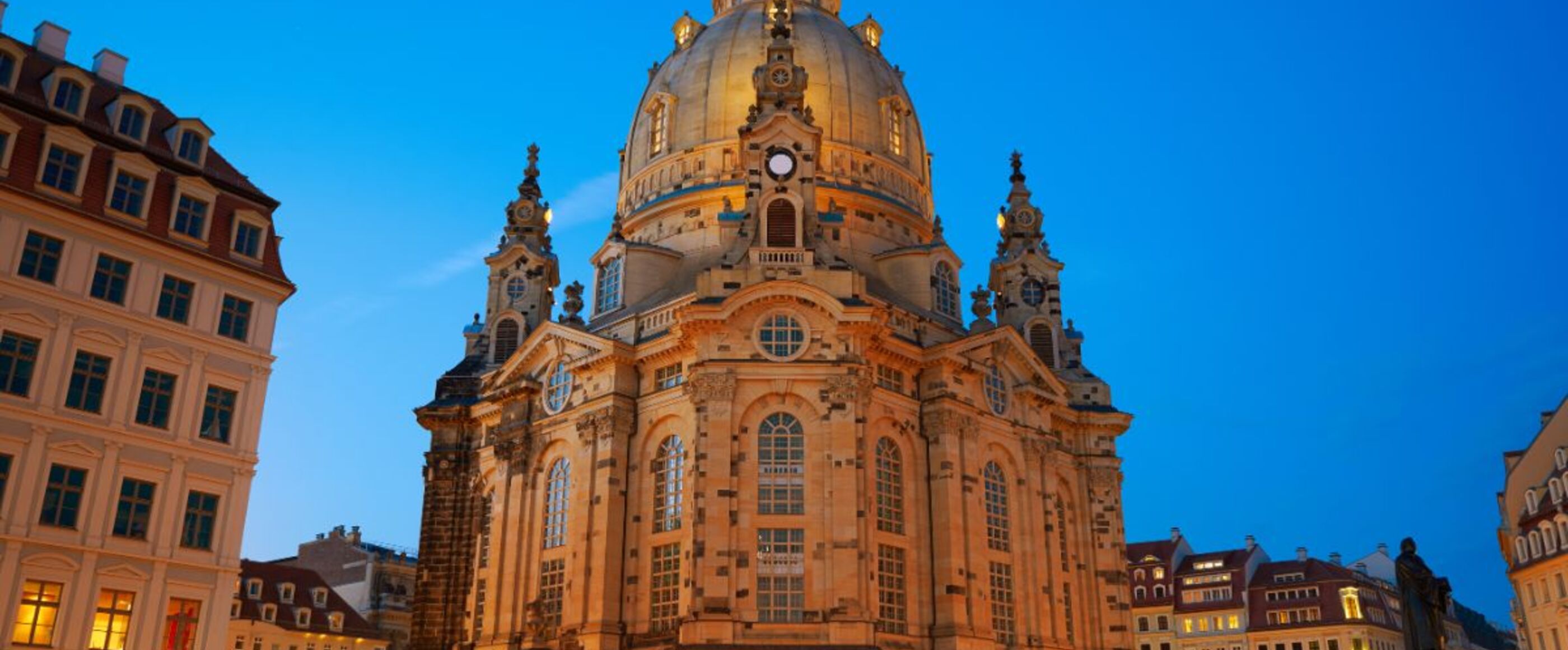 Die Frauenkirche Dresden erhebt sich gegen den blau leuchtenden Himmel. Von unten leuchten die Kirche und umliegenden Häuser golden im Licht der Laternen.