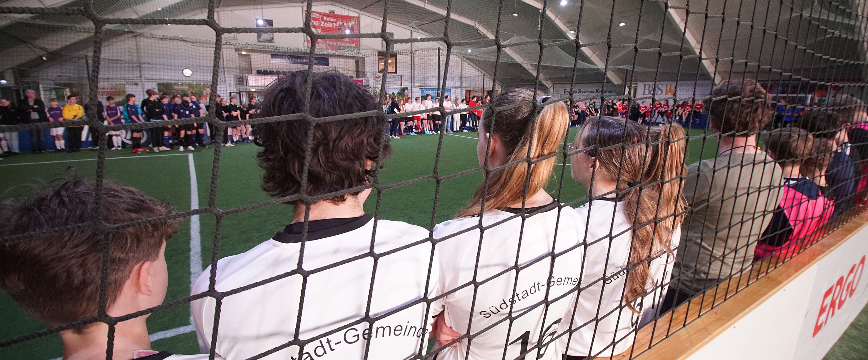 Mehrere Jugendliche stehen in Fußballkleidung in einer Halle hinter einem Netz.